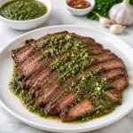 Juicy garlic butter flank steak served with chimichurri sauce on a plate.